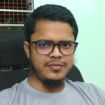 Man wearing glasses and a gray shirt against a light green wall.